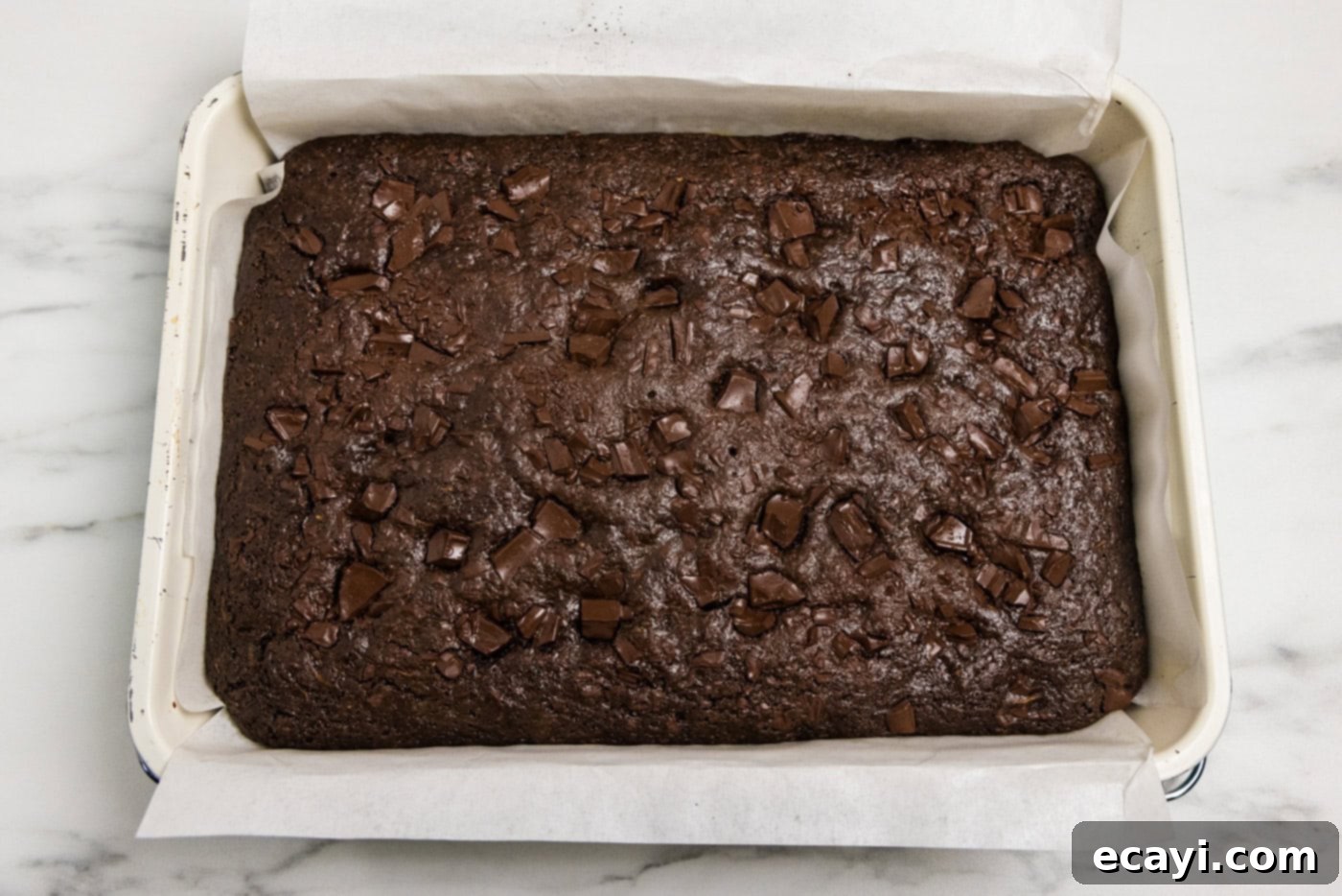 Hidden Veggie Fudge 12 Pan of baked zucchini brownies with parchment paper over the side, freshly out of the oven