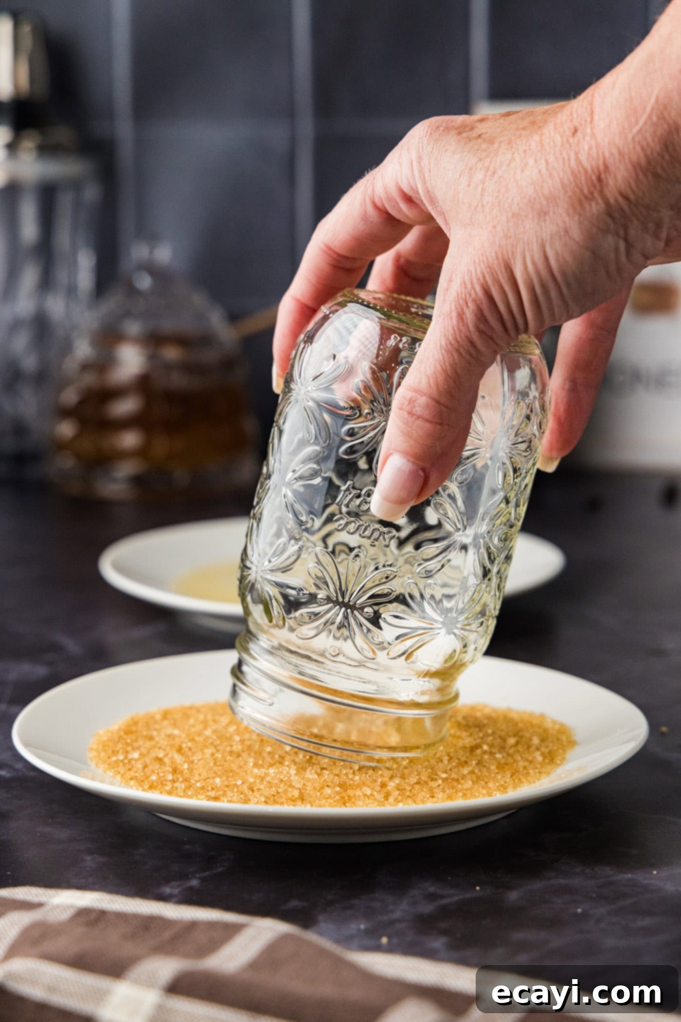 Velvet Espresso Chill 5 A hand carefully dipping the rim of a drinking glass into a saucer filled with turbinado sugar to create a decorative sugar rim.