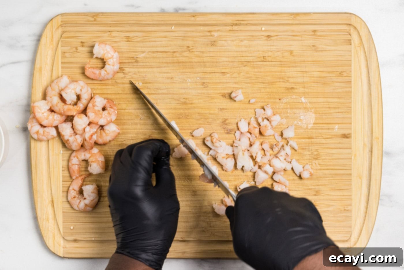 Creamy Shrimp Delight 5 Hands using a knife to chop up cooked shrimp on a cutting board into small pieces