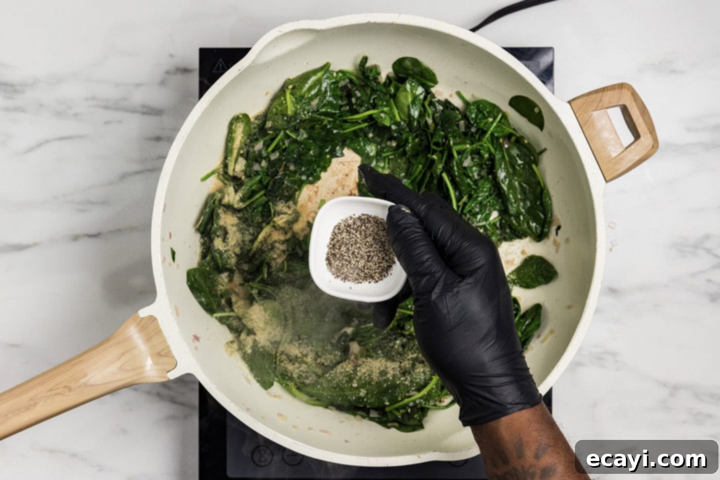 Vibrant Spinach Spaghetti 6 Overhead photo of a hand adding black pepper to the wilting spinach mixture in a skillet.