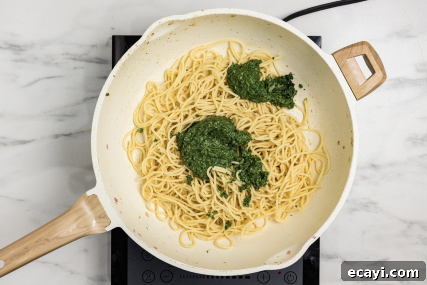 Vibrant Spinach Spaghetti 10 Spinach sauce being added to a skillet with cooked spaghetti noodles.