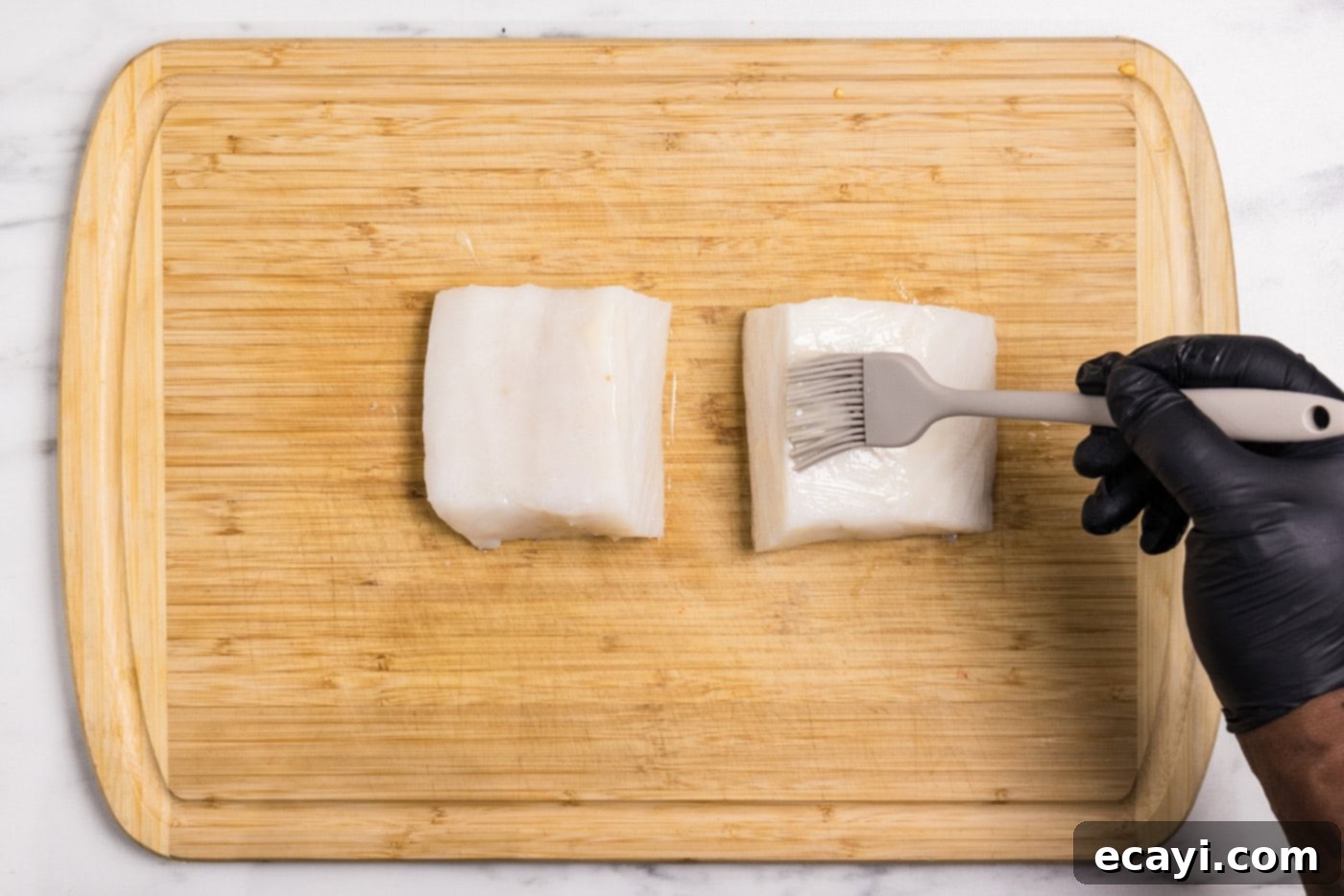 Buttery Grilled Chilean Sea Bass 5 A basting brush applying melted butter evenly onto raw Chilean sea bass fillets on a cutting board.
