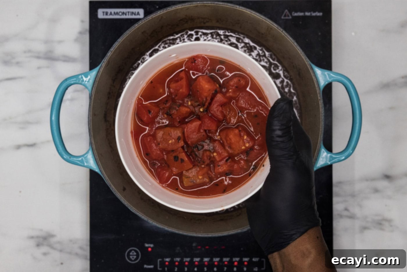 Fork-Tender Short Rib Chili 9 hand holding diced tomatoes in a bowl over dutch oven with braising liquid, preparing for the slow simmer