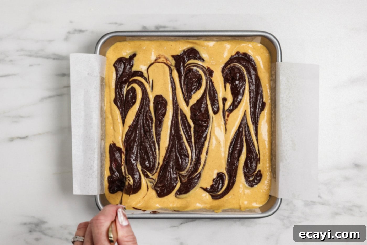 Spiced Pumpkin Cheesecake Swirl Brownies 14 hand using a butter knife to drag spoonfuls of brownie batter over pumpkin cheesecake layer
