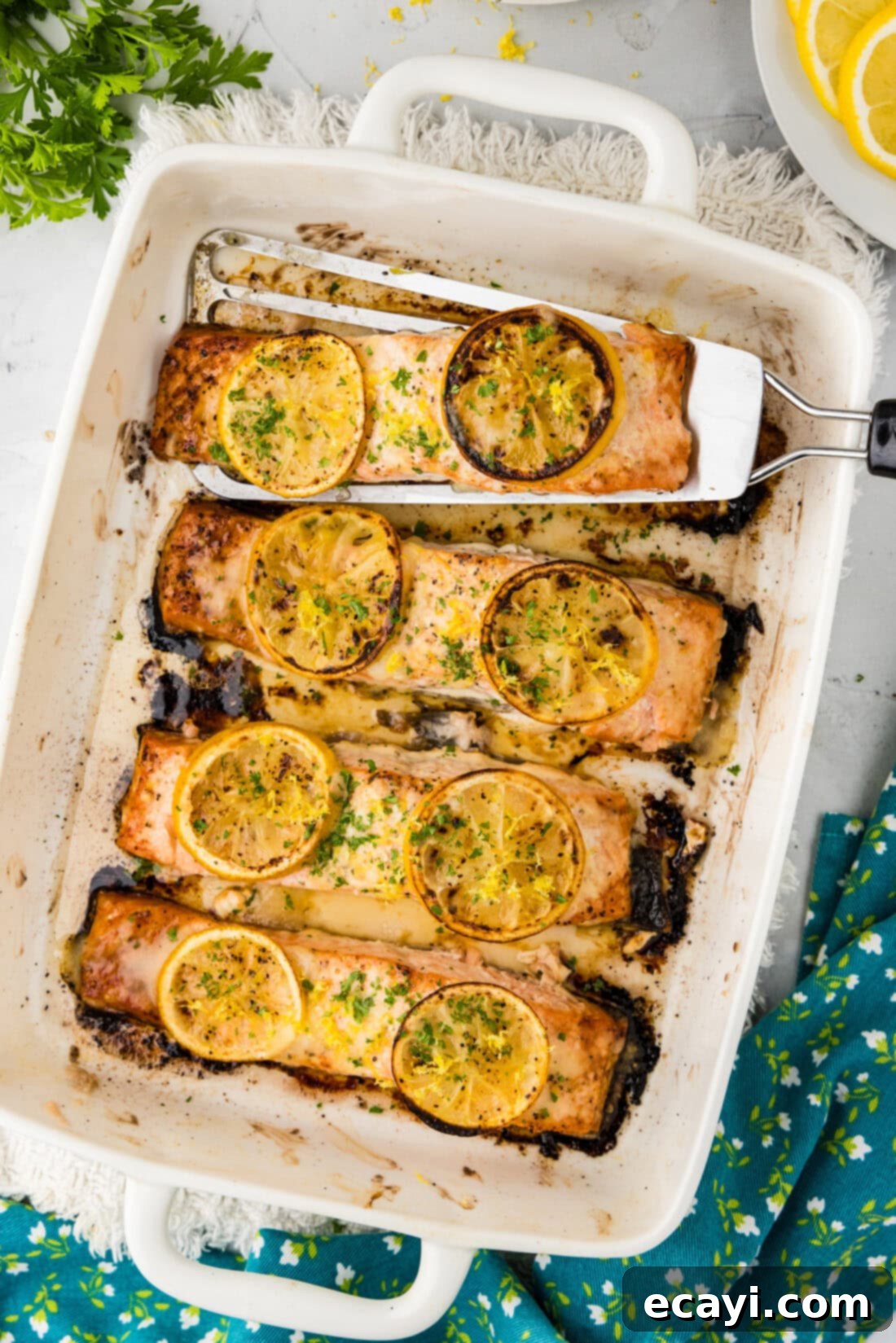 Zesty Lemon Salmon Bake 2 Baking dish of Baked Lemon Salmon with a filet being removed, showcasing its tender, flaky texture and bright lemon slices.