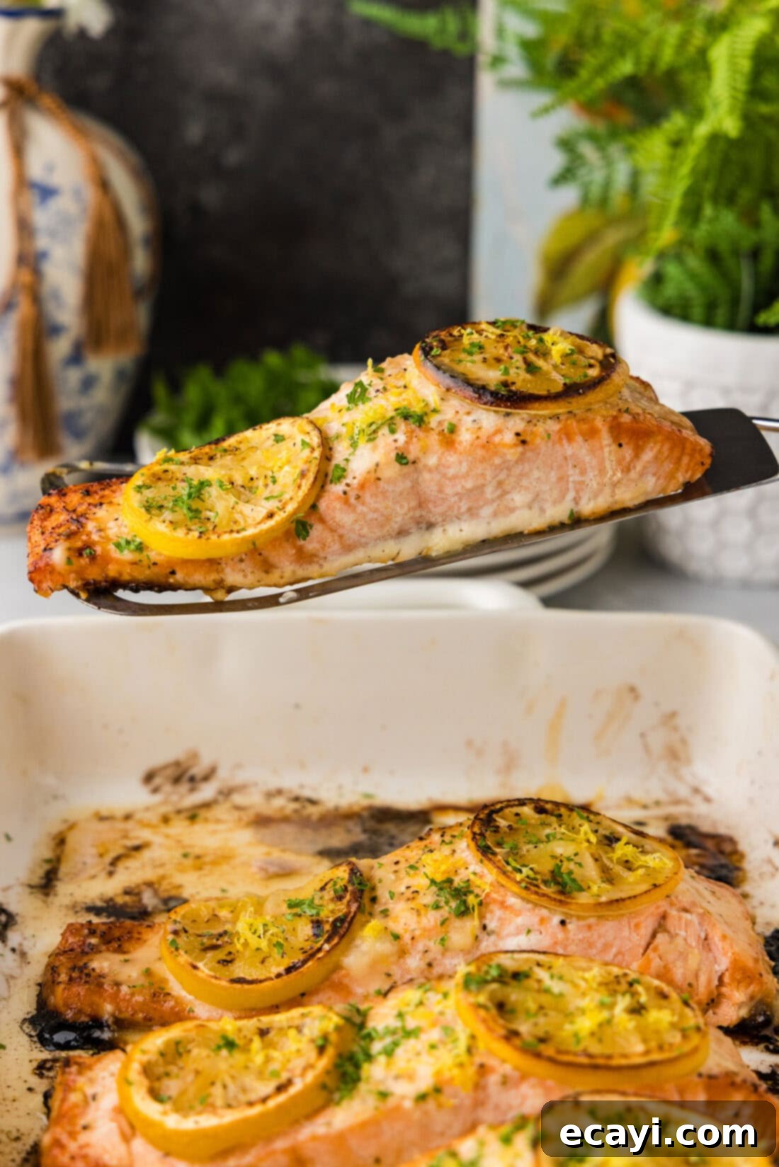 Zesty Lemon Salmon Bake 3 A perfectly cooked filet of Baked Lemon Salmon being lifted from a baking dish, glistening with lemon butter sauce and adorned with fresh lemon slices.