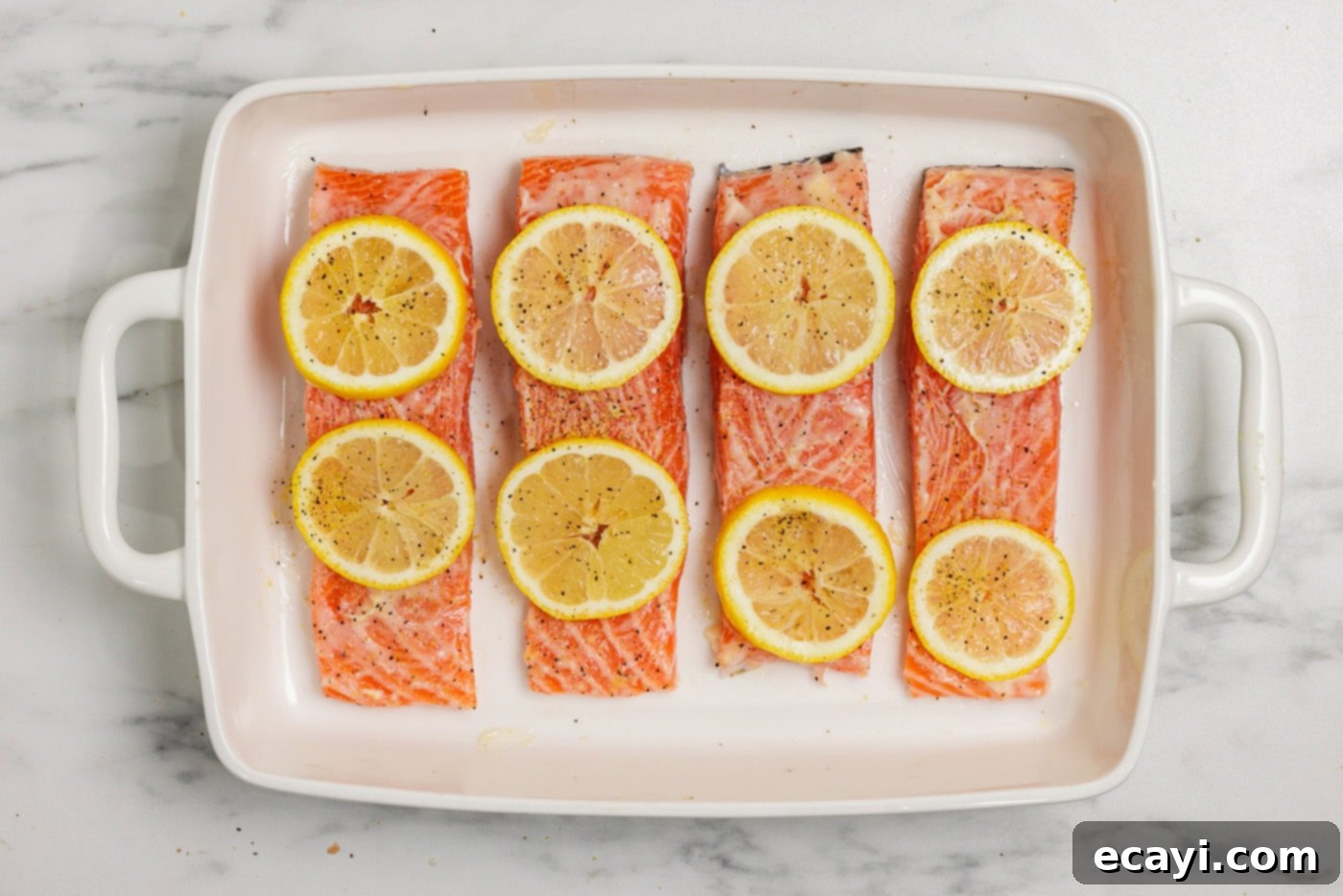 Zesty Lemon Salmon Bake 5 Salmon filets generously topped with lemon butter and vibrant sliced lemons, nestled in a baking dish, ready for the oven.