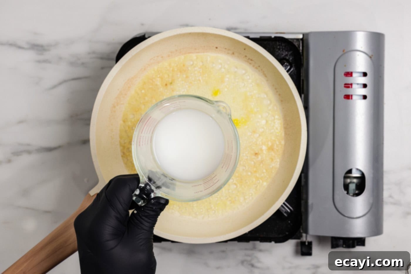 Zesty Lemon Salmon Bake 6 A hand holding a measuring cup, carefully drizzling a cornstarch slurry into a simmering skillet of lemon butter sauce, illustrating the thickening process.