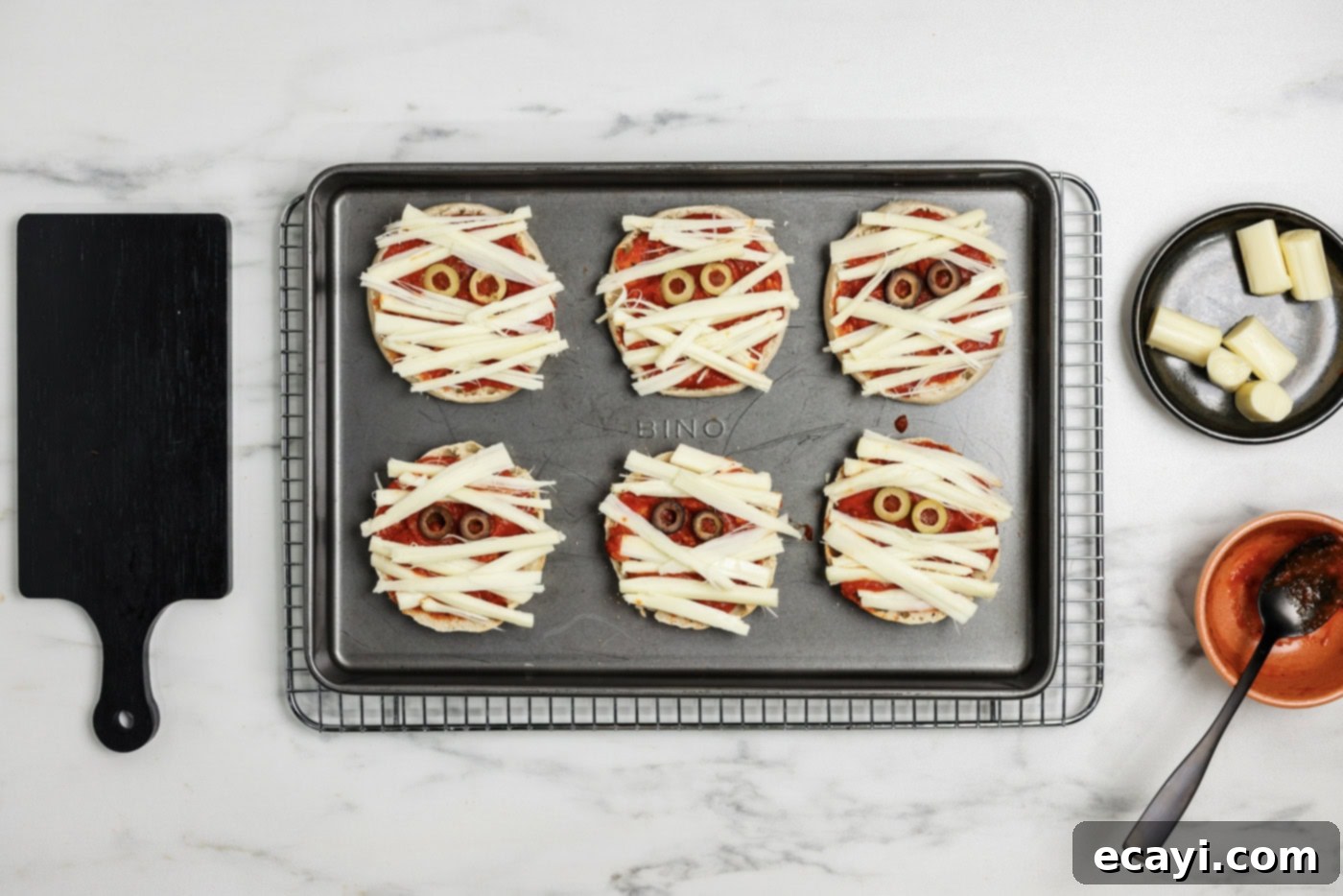 Mummy Mini Pizza Bites 8 strips of cheese on top of English Muffins with sliced olive eyes to look like mummies