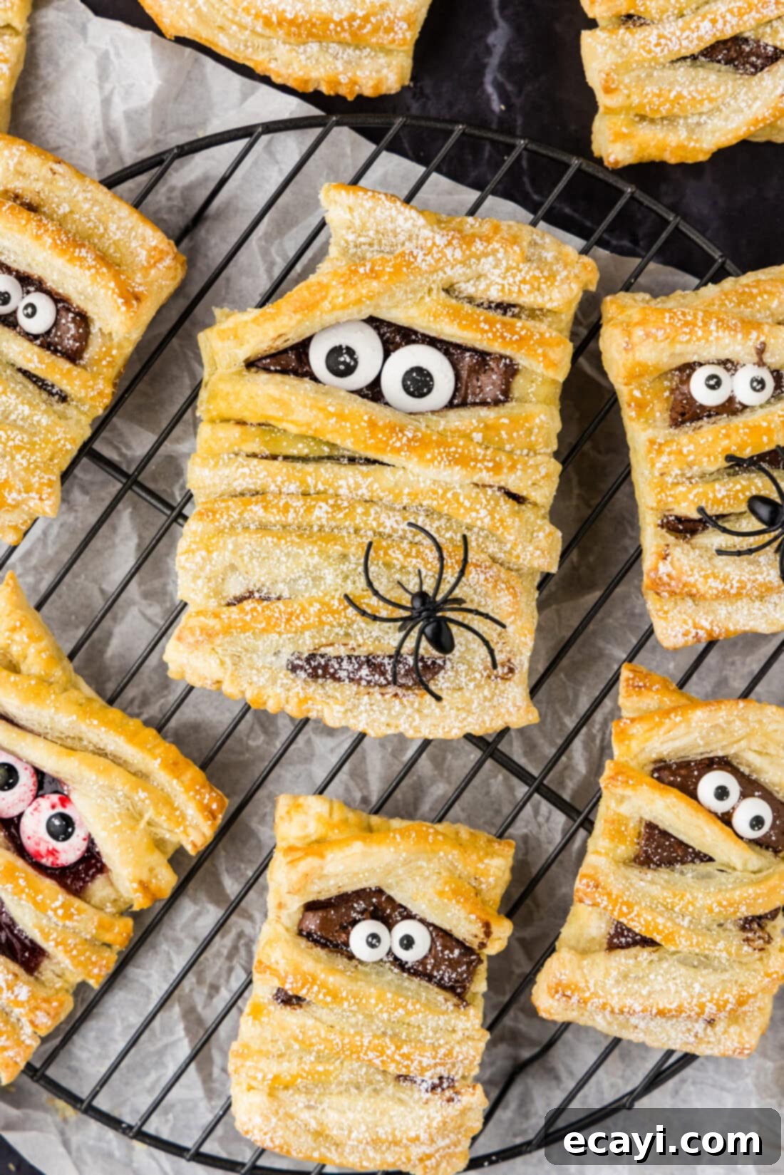 Halloween Mummy Bites 2 Close up photo of Mummy Hand Pies with a bite taken out of one, revealing a sweet, red jam filling.