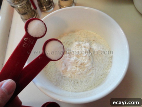homemade-chicken-nuggets-step-6 A close-up shot of salt being poured from a small spoon into a bowl filled with white all-purpose flour, ready to be mixed.