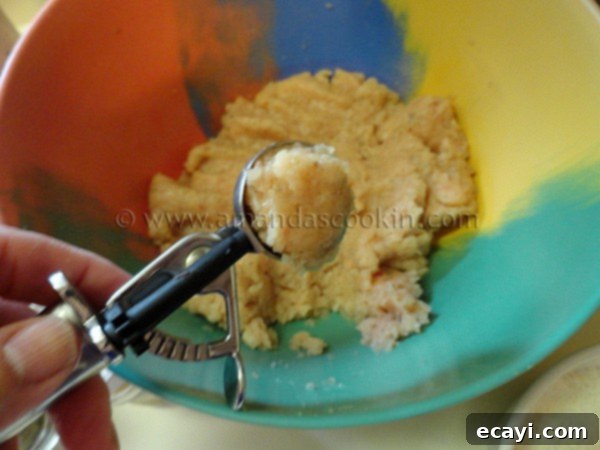 homemade-chicken-nuggets-step-7 A metal cookie scoop holds a portion of raw, seasoned chicken mixture, perfectly shaped into a ball.