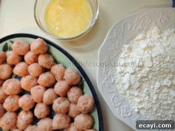 homemade-chicken-nuggets-step-8 A clean, organized setup for breading chicken nuggets, featuring a plate of raw chicken balls, a bowl of whisked eggs, and a plate of seasoned flour.