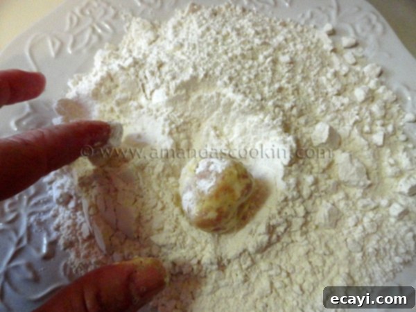 homemade-chicken-nuggets-step-11 A chicken ball, already coated in egg, being rolled in the flour mixture for a second time, creating a thick, crispy breading.