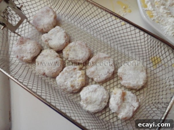 homemade-chicken-nuggets-step-14 Raw, breaded chicken nuggets neatly arranged in a metal frying basket, prepared for deep frying.