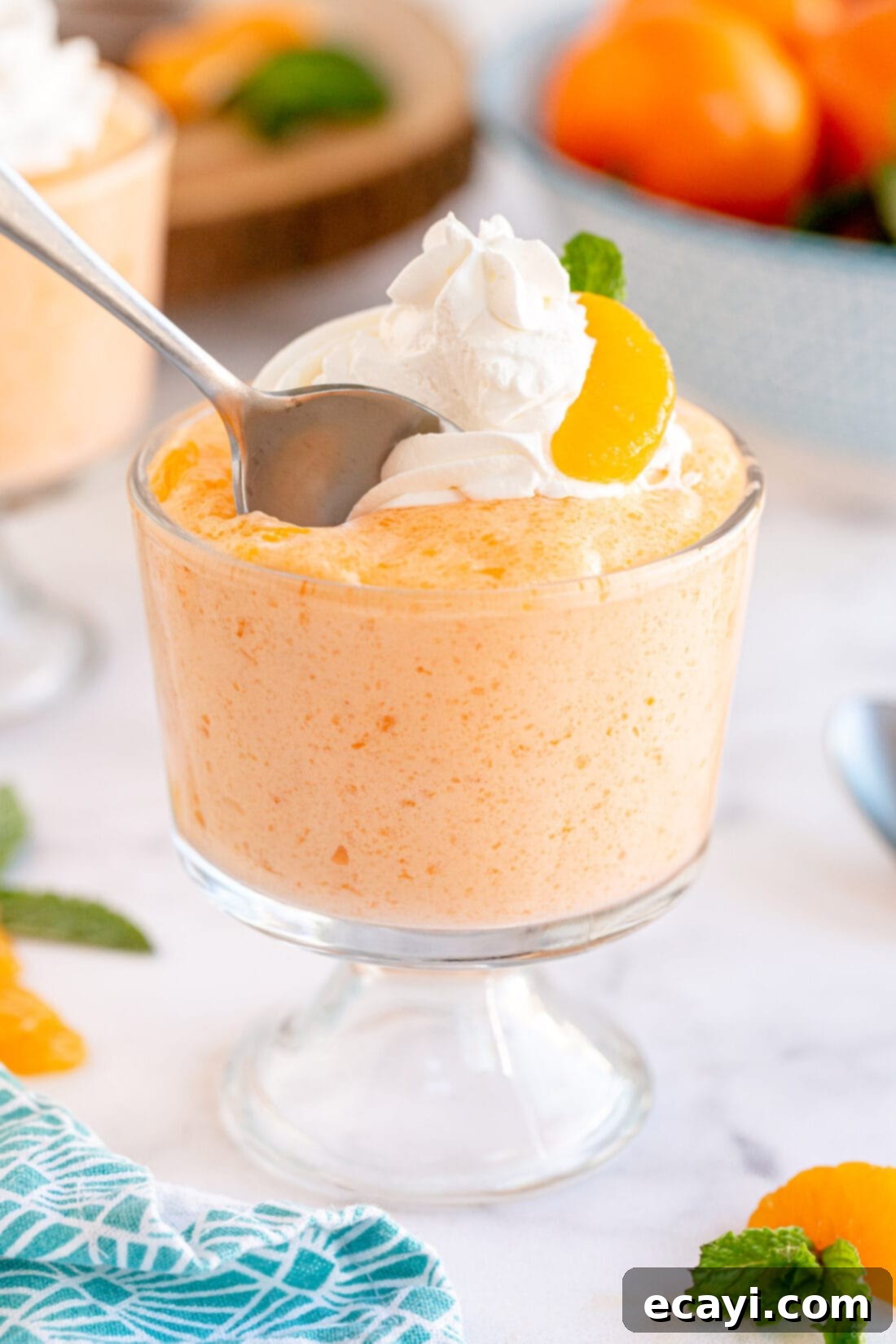 Sunshine Mandarin Whipped Mousse 3 A delicate spoon scoops into a glass cup of airy mandarin orange whipped jello mousse.