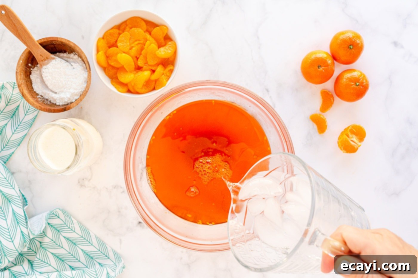 Sunshine Mandarin Whipped Mousse 6 Ice water being poured into a bowl of warm gelatin mixture, stirring to cool it rapidly.