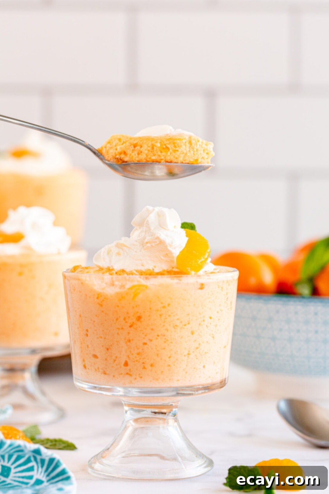 Sunshine Mandarin Whipped Mousse 9 Close-up of a spoon lifting a portion of fluffy mandarin orange whipped jello mousse from a glass cup, showing its smooth texture.