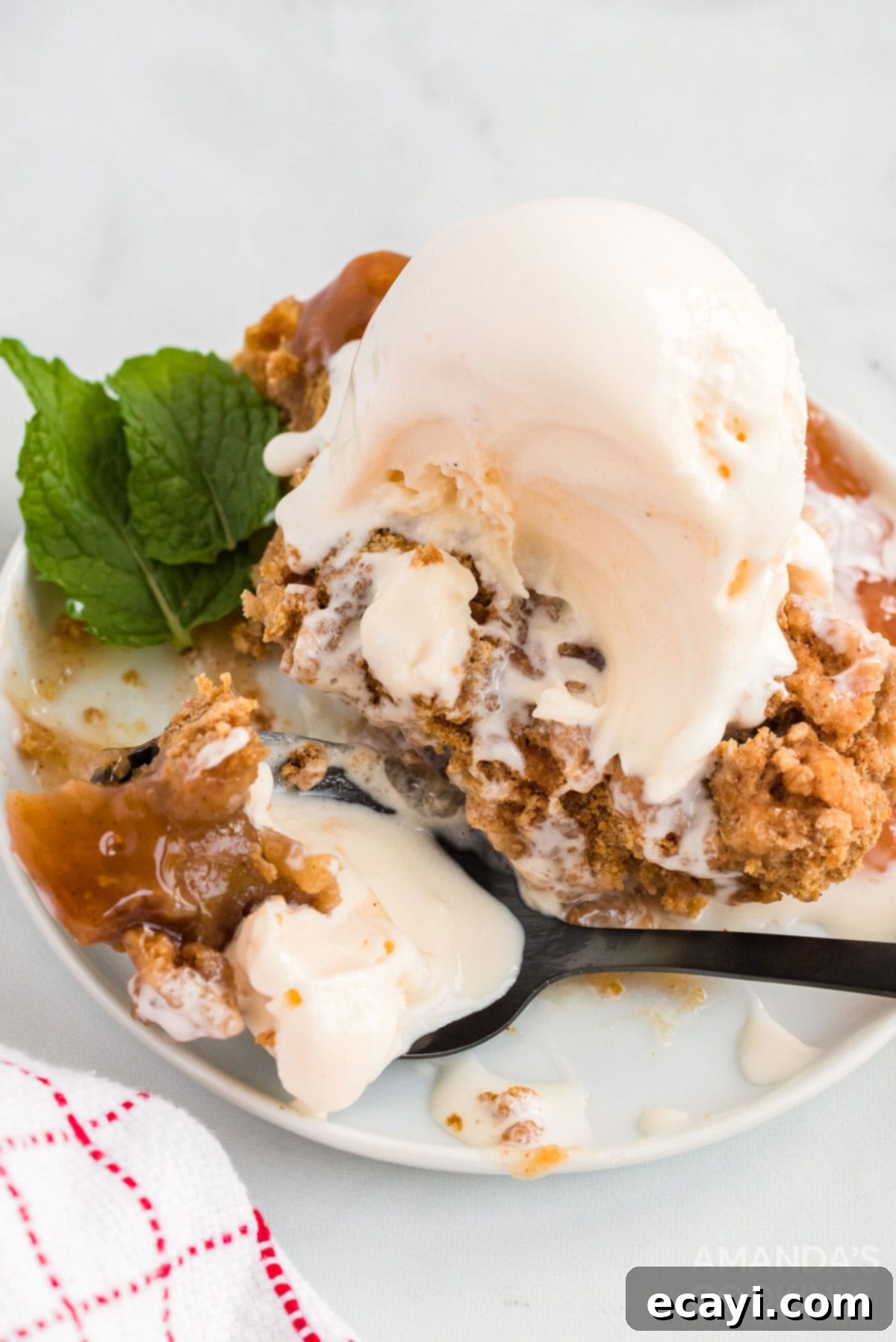 Make crockpot apple cobbler in your slow cooker. This easy crockpot dessert is quick & simple and great any time of year. A slice of warm apple cobbler topped with a scoop of melting vanilla ice cream on a white plate.