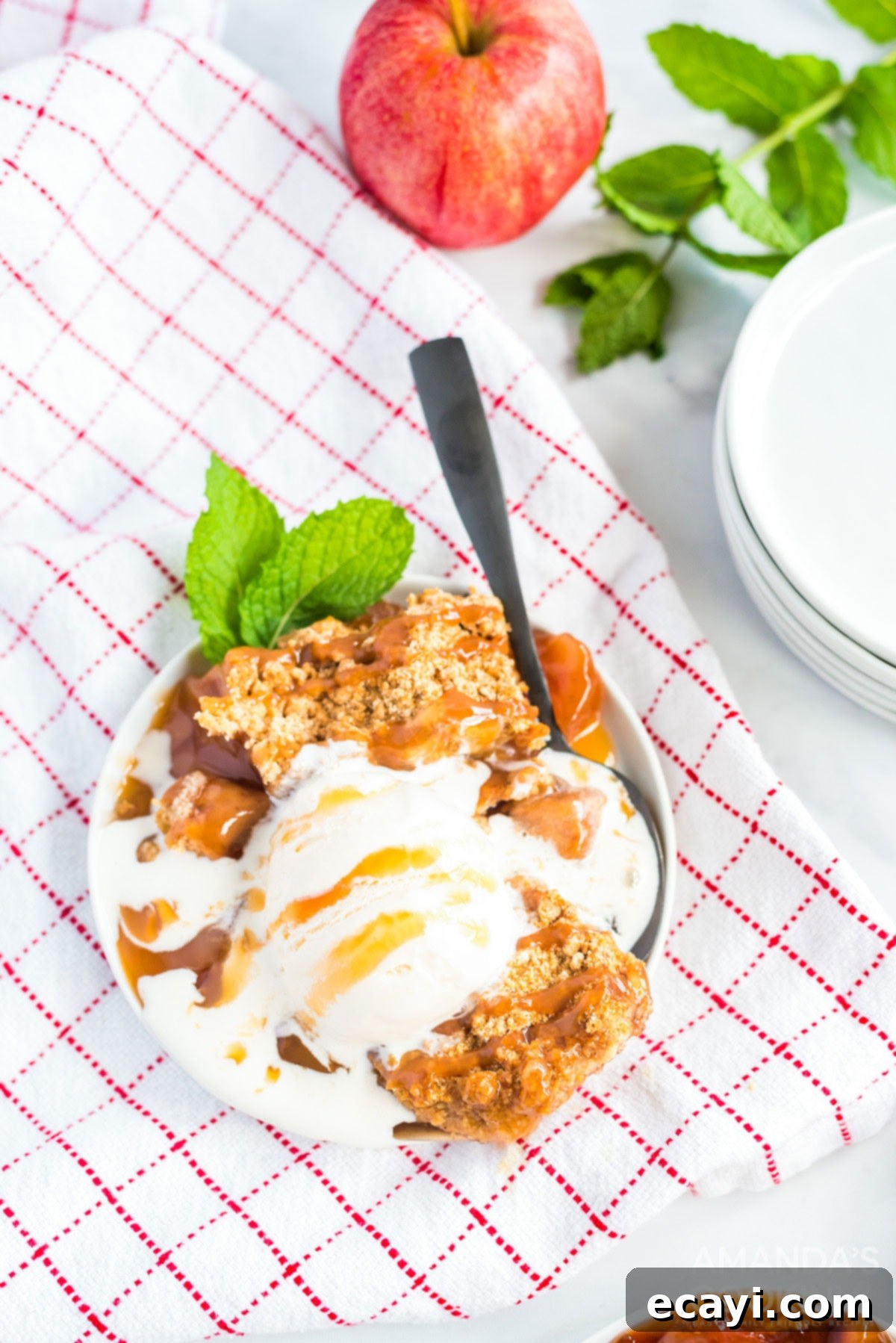 Cozy Apple Cobbler 2 Crockpot apple cobbler served with vanilla ice cream on a plate placed on a checkered kitchen towel.