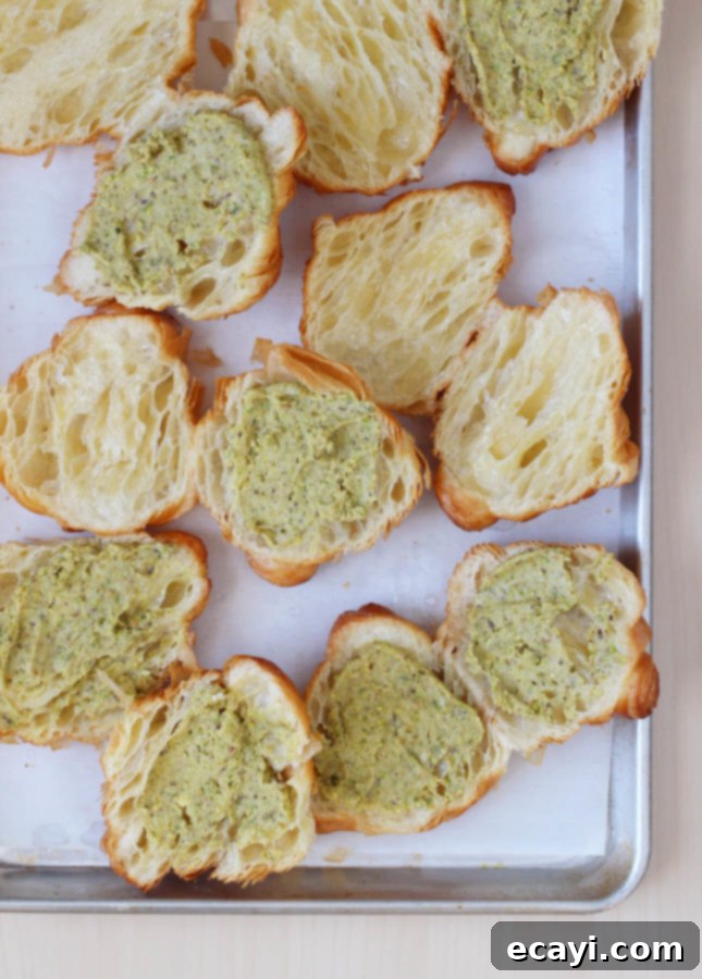 Effortless Pistachio Croissant Indulgence 3 Homemade Pistachio Croissants on a baking sheet, featuring bright green pistachio frangipane and a dusting of powdered sugar.