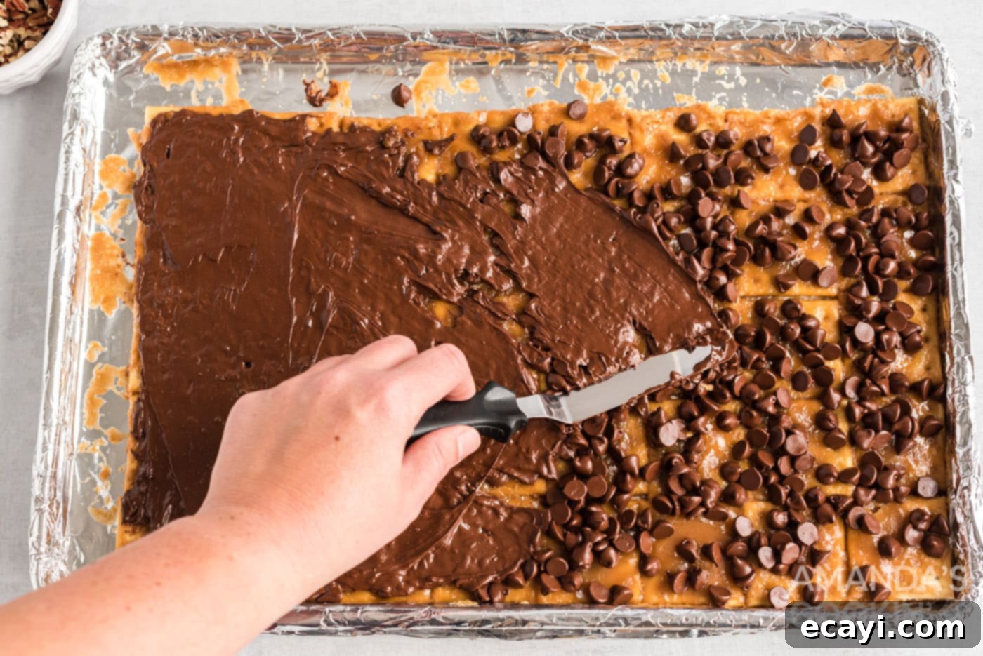 Salty Sweet Toffee Crunch 11 spatula spreading melted chocolate over saltine toffee