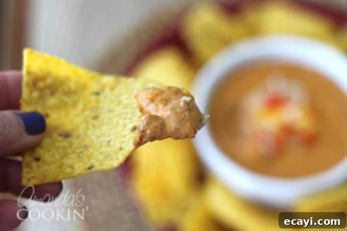 Creamy, cheesy chili dip ready for your next party! close up of chili cheese dip on a tortilla chip