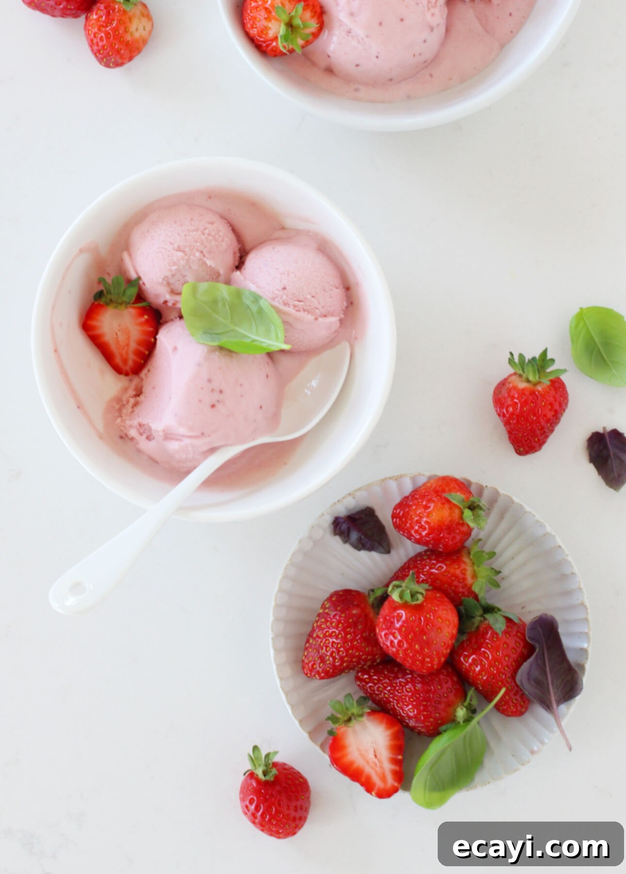 Basil-Kissed Strawberry White Chocolate Gelato 3 A close-up of a serving of white chocolate, strawberry, and basil gelato in a glass bowl, garnished with fresh basil leaves. This homemade gelato recipe features sweet strawberries and aromatic basil for a refreshing summer treat from FoodNouveau.com.