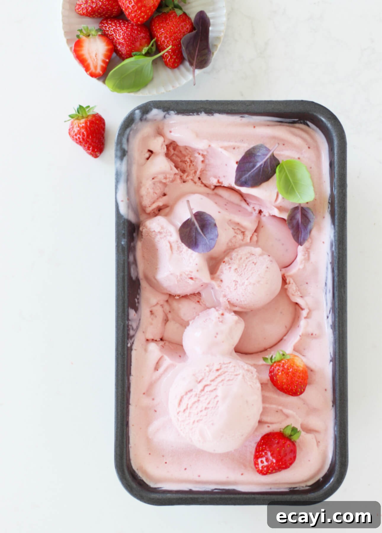 Basil-Kissed Strawberry White Chocolate Gelato 6 Three bowls of luscious pink white chocolate, strawberry, and basil gelato, artfully garnished with fresh strawberries and basil leaves, are elegantly arranged on a white surface alongside a small dish of berries and three elegant spoons, ready to be enjoyed.