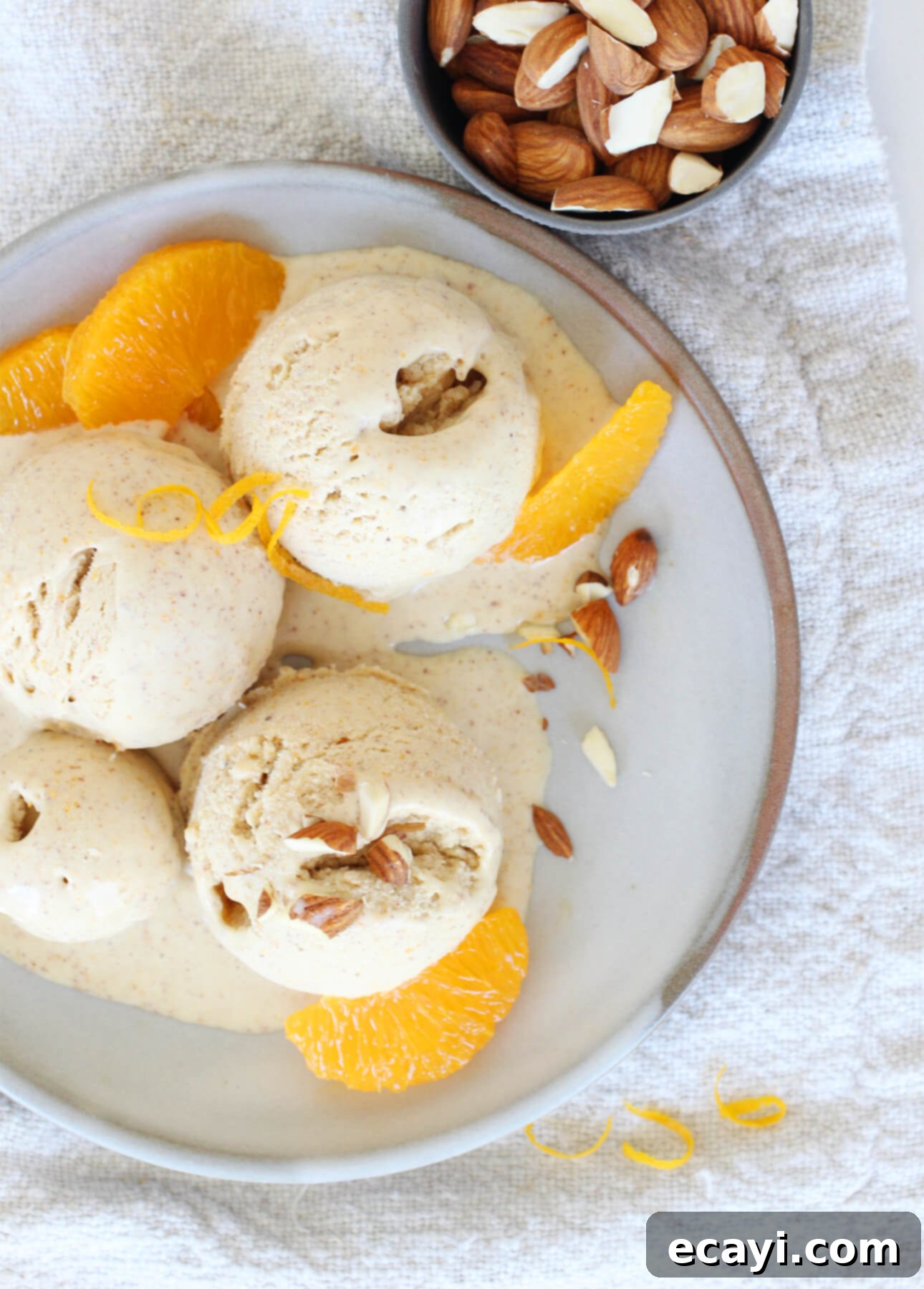 Crafting Creamy Vegan Gelato at Home 9 Scoops of vibrant orange almond vegan gelato are garnished with sliced almonds and fresh orange segments on a plate, showcasing a delicate plant-based flavor base. // FoodNouveau.com