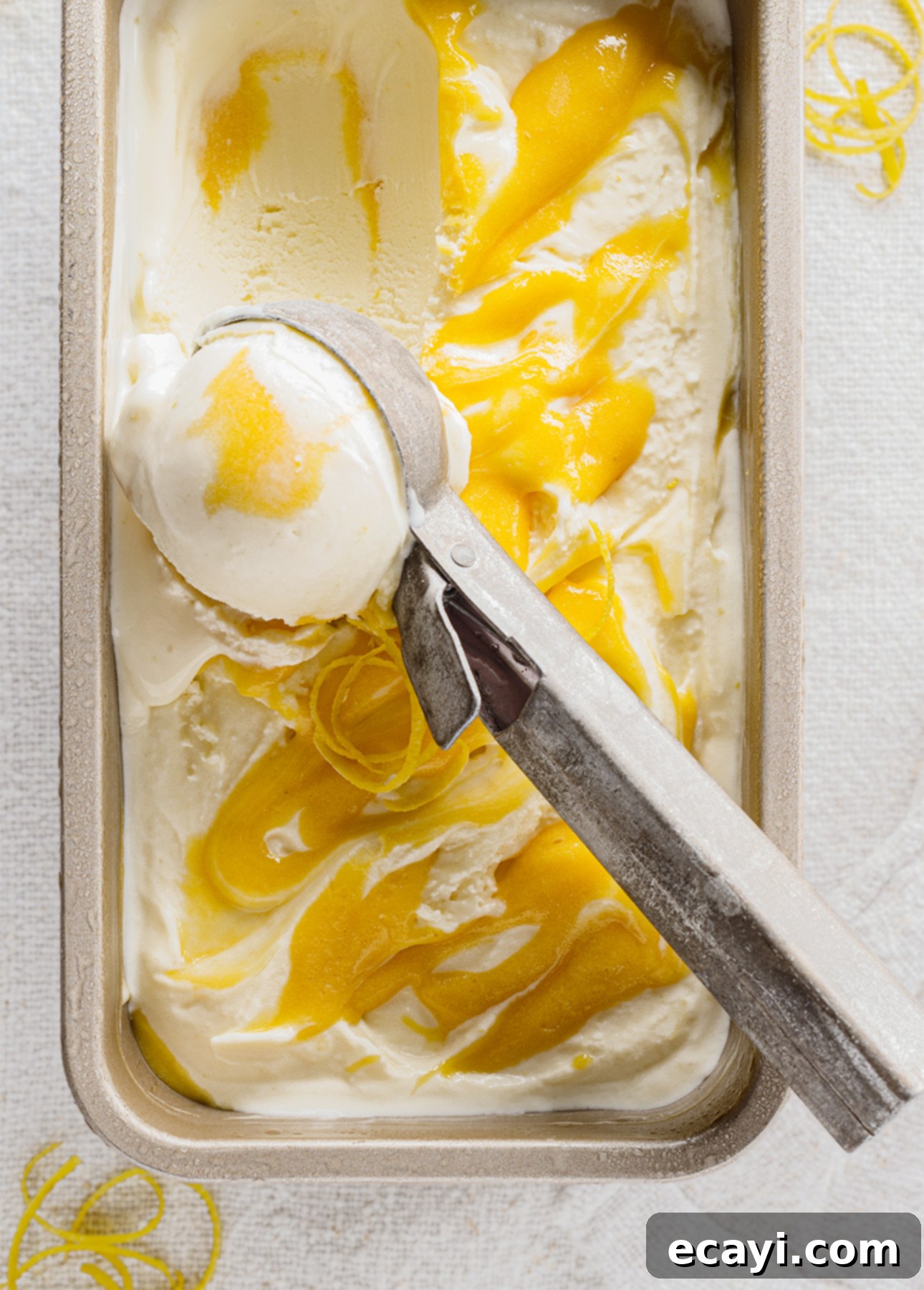 Crafting Creamy Vegan Gelato at Home 10 A rectangular dish brimming with creamy white lemon vegan gelato swirled with vibrant lemon curd. An ice cream scoop sits on top, ready to serve the perfectly tempered plant-based treat. // FoodNouveau.com