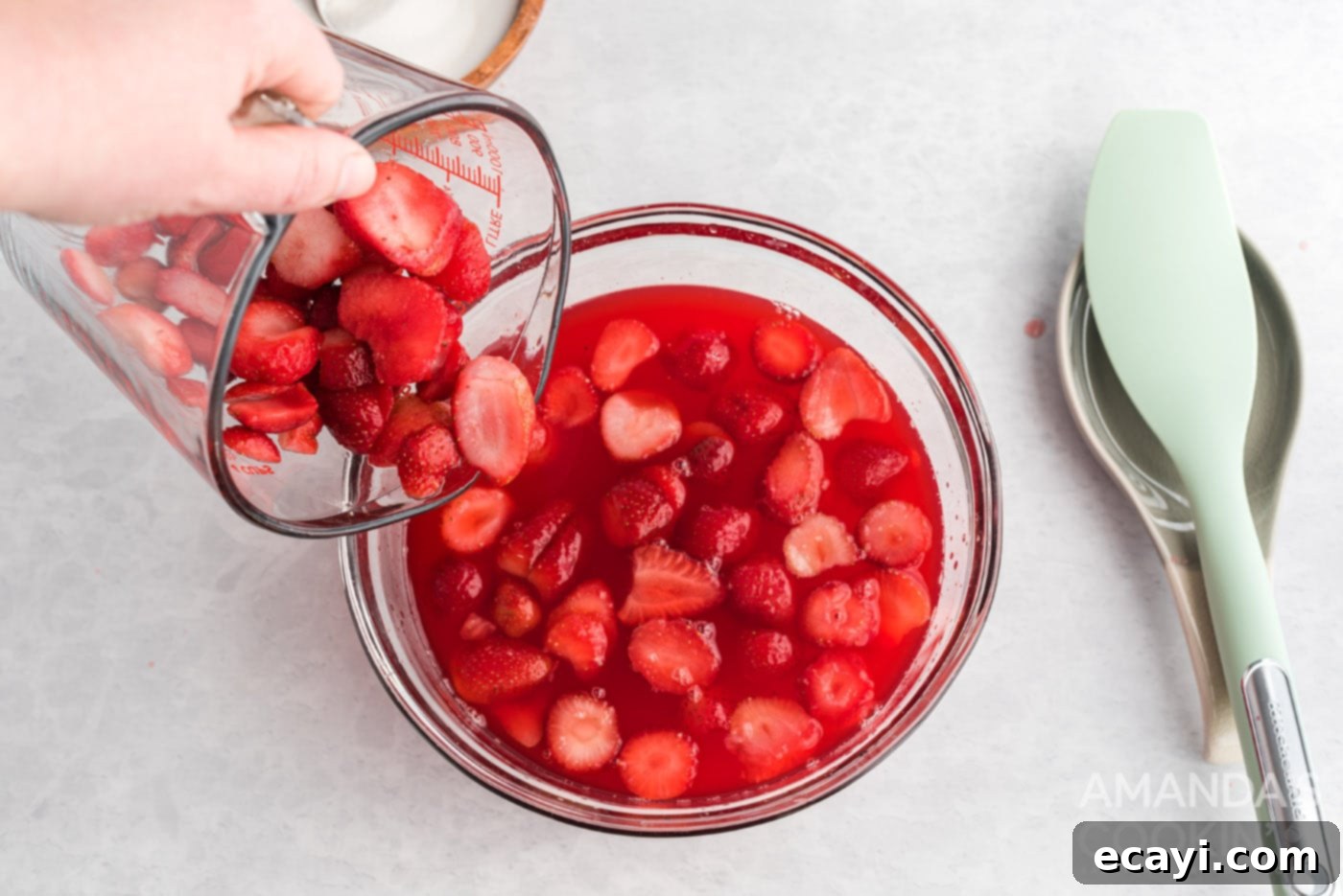 Strawberry Pretzel Delight 9 Gently pouring sliced fresh strawberries into a dish containing the partially prepared strawberry gelatin.