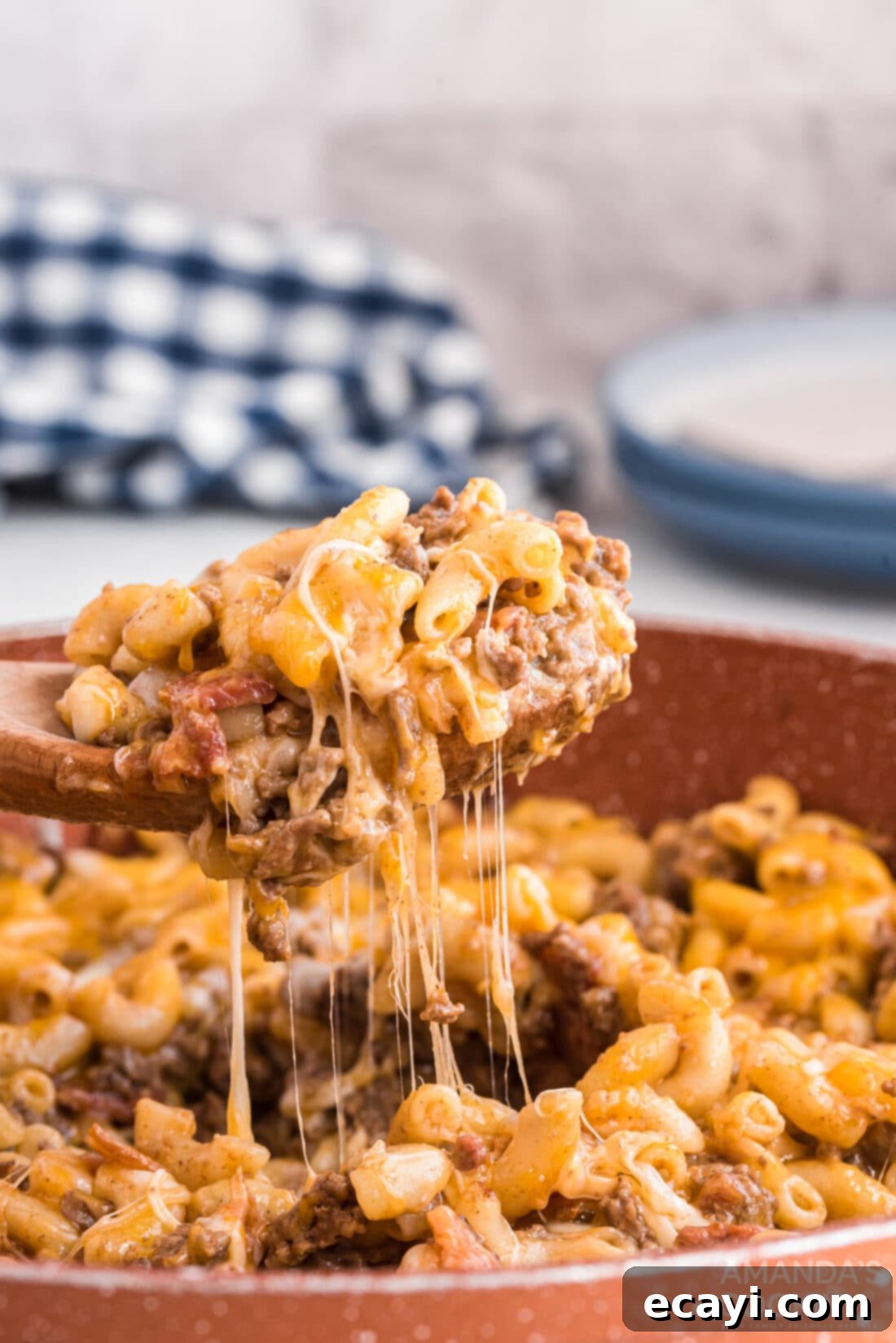 Ultimate Bacon Cheeseburger Bake 2 A spoon lifting a portion of warm, cheesy bacon cheeseburger casserole from a skillet, showing the macaroni, ground beef, and melted cheese.