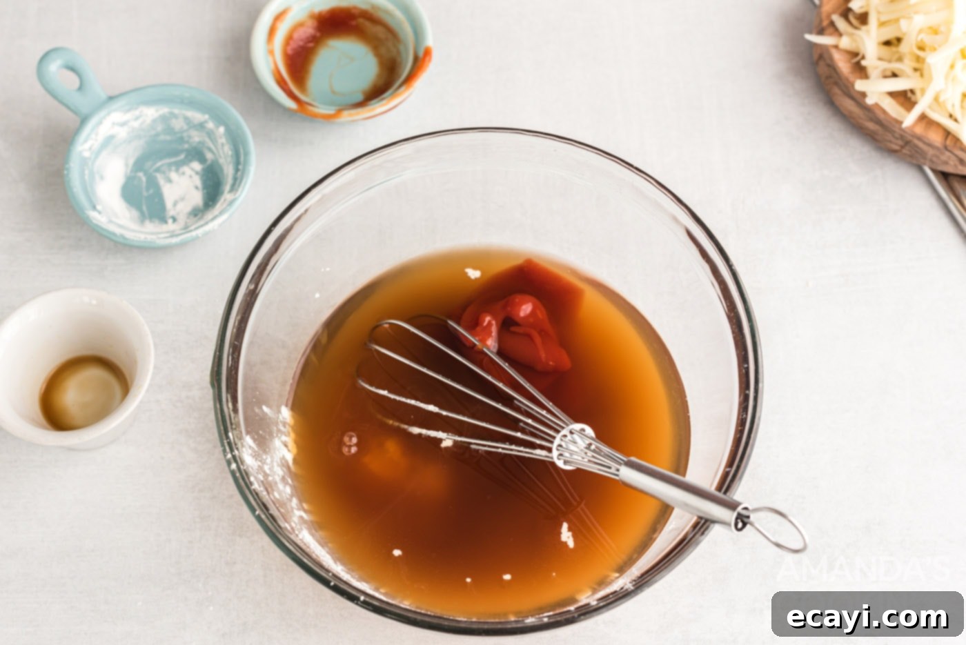 Ultimate Bacon Cheeseburger Bake 5 A bowl containing ketchup, Worcestershire sauce, and beef broth, with a whisk ready to combine ingredients for the casserole sauce.