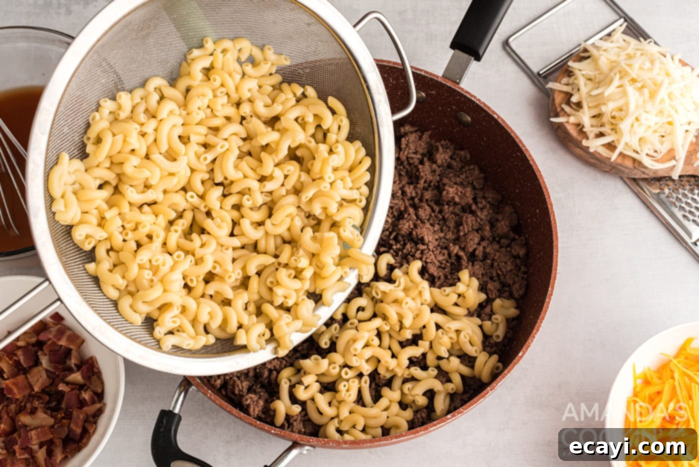 Ultimate Bacon Cheeseburger Bake 6 Drained elbow macaroni being poured over the cooked ground beef mixture in a skillet, ready for the sauce.