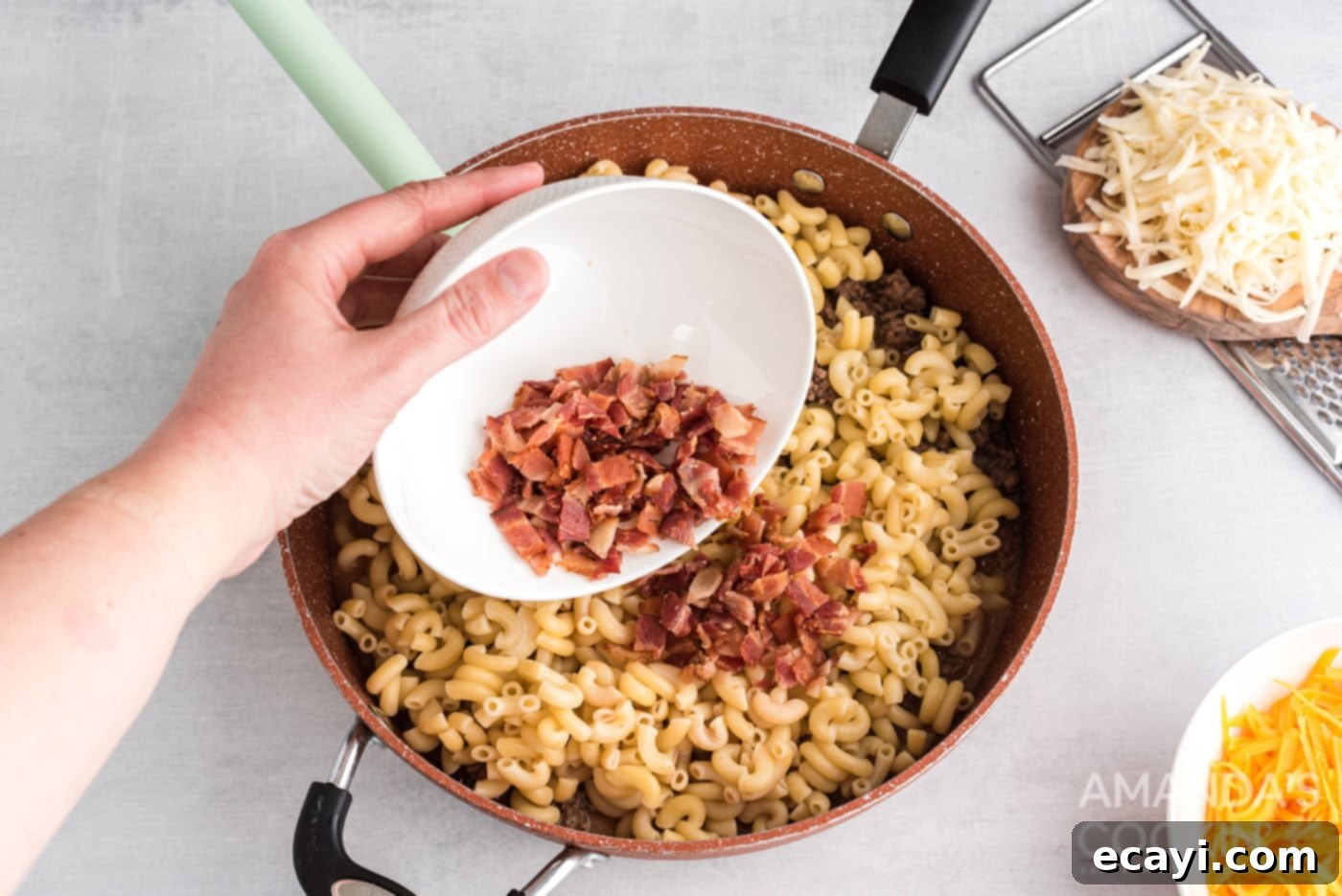 Ultimate Bacon Cheeseburger Bake 8 Crispy bacon bits being added to the skillet with the pasta and ground beef mixture, for a rich, smoky flavor.