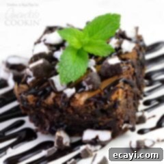 Peppermint Patty Fudge Brownies 8 A close up photo of a peppermint patty brownie topped with drizzled chocolate sauce, chopped peppermint patties and a mint leaf, showcasing its delicious appeal.