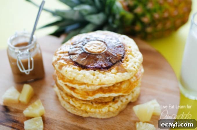 Tropical Pineapple Pancakes with Homemade Coconut Bliss 4 A stack of golden brown pineapple pancakes, ready to be served, on a rustic wooden surface.