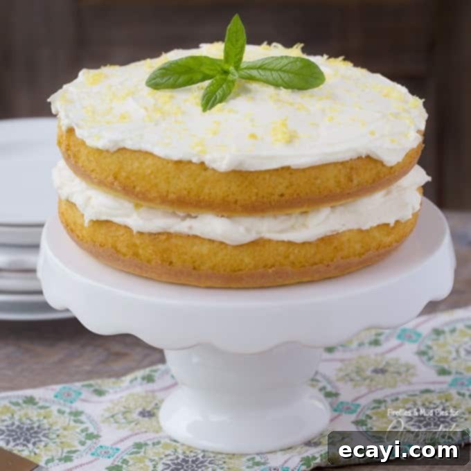Luscious Lemon Curd Poke Cake 2 A close up of a lemon curd poke cake on a white cake stand topped with fresh mint leaves and grated lemon peel, showcasing its vibrant yellow color and elegant presentation.