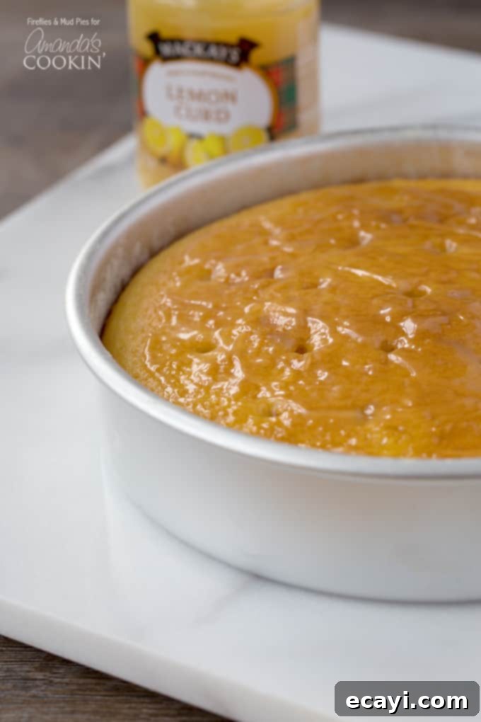 Luscious Lemon Curd Poke Cake 3 A close up photo of a fresh baked lemon curd poke cake resting in a round cake pan, showing the golden-brown crust and moist interior before frosting. The holes are already poked in the top.