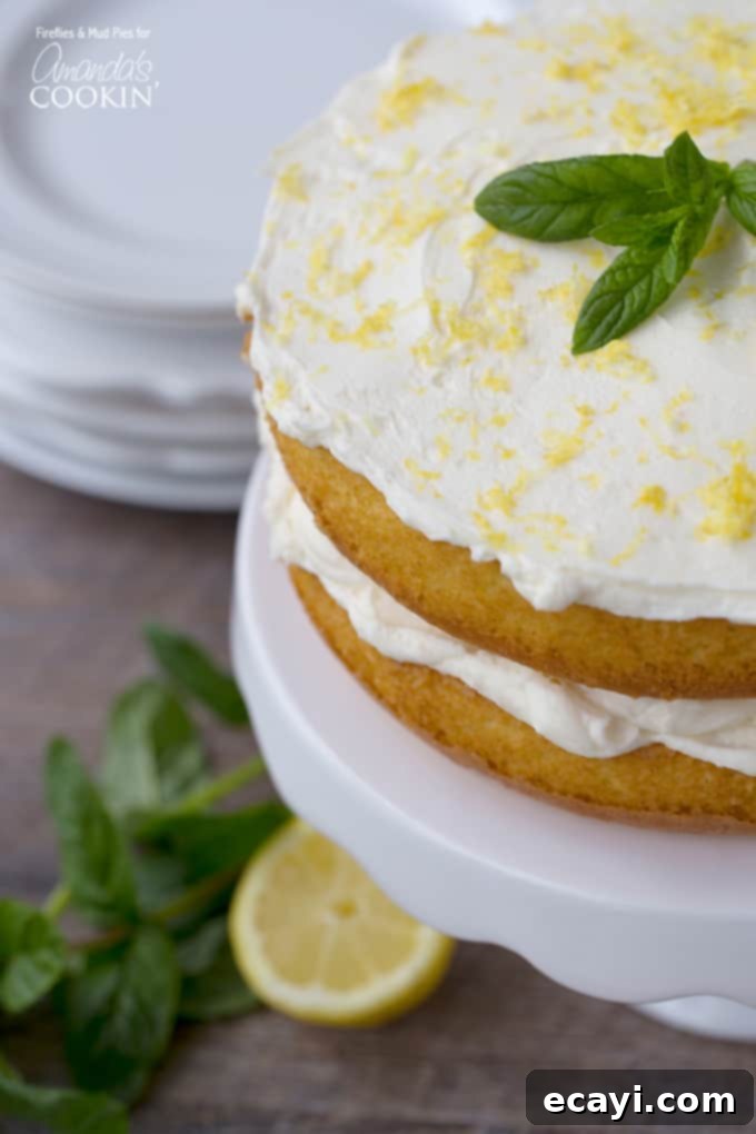 Luscious Lemon Curd Poke Cake 4 A close up of a fully assembled lemon curd poke cake on a white cake stand, richly frosted and elegantly garnished with vibrant fresh mint leaves and fine lemon zest, ready to be served and enjoyed.