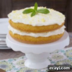 Luscious Lemon Curd Poke Cake 7 A close up of a beautiful lemon curd poke cake on a white cake stand, garnished with fresh mint leaves and lemon zest.