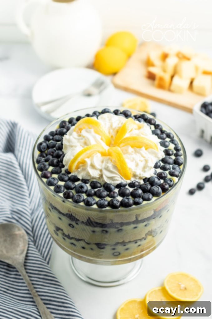 Overhead view of a delectable Lemon Blueberry Trifle with fresh fruit garnish. An overhead view of a lemon blueberry trifle, showcasing the top layer of whipped cream, abundant fresh blueberries, and delicate lemon slices used as garnish. The clear trifle bowl reveals the distinct layers beneath.