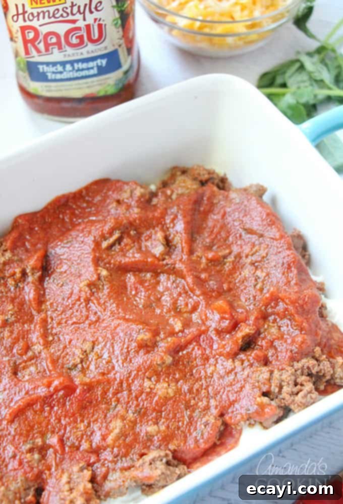 Pizzagna 11 An overhead photo of Ragu Homestyle pasta sauce being poured generously over the layers of ground beef, pepperoni, ricotta, and lasagna noodles in a dish.