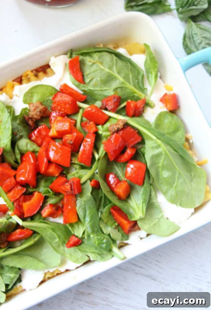 Pizzagna 13 A photo of creamy ricotta cheese spread on lasagna noodles, fresh spinach over that, and colorful chopped red bell peppers on top.