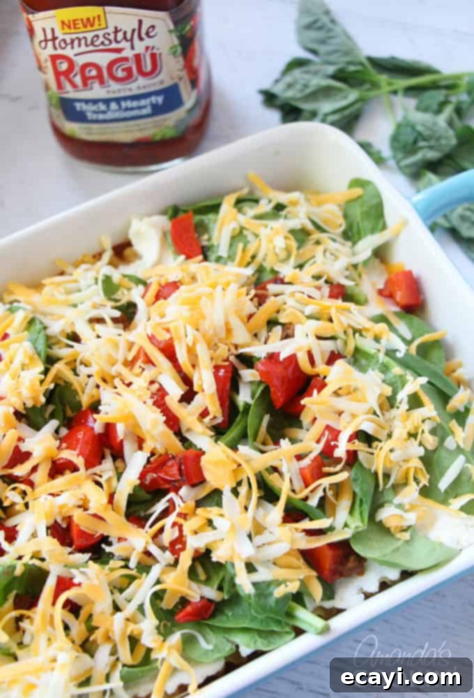 Pizzagna 14 A photo of golden shredded cheese sprinkled over a layer of fresh vegetables in the lasagna dish.