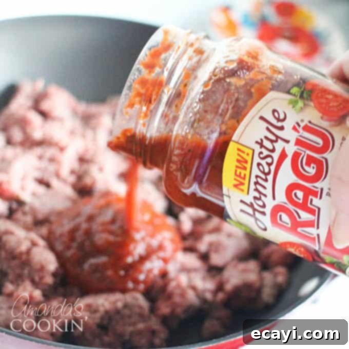 Pizzagna 6 A close up photo of Ragu sauce being poured into a skillet of browned ground beef.