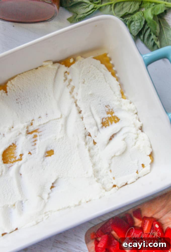 Pizzagna 8 An overhead photo of lasagna noodles in a pan with creamy ricotta cheese generously spread on top.