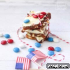 Stars and Stripes Candy Bark 5 4th of July M&M bark stacked on top of each other with American flags and red, white and blue M&Ms scatted in the background.