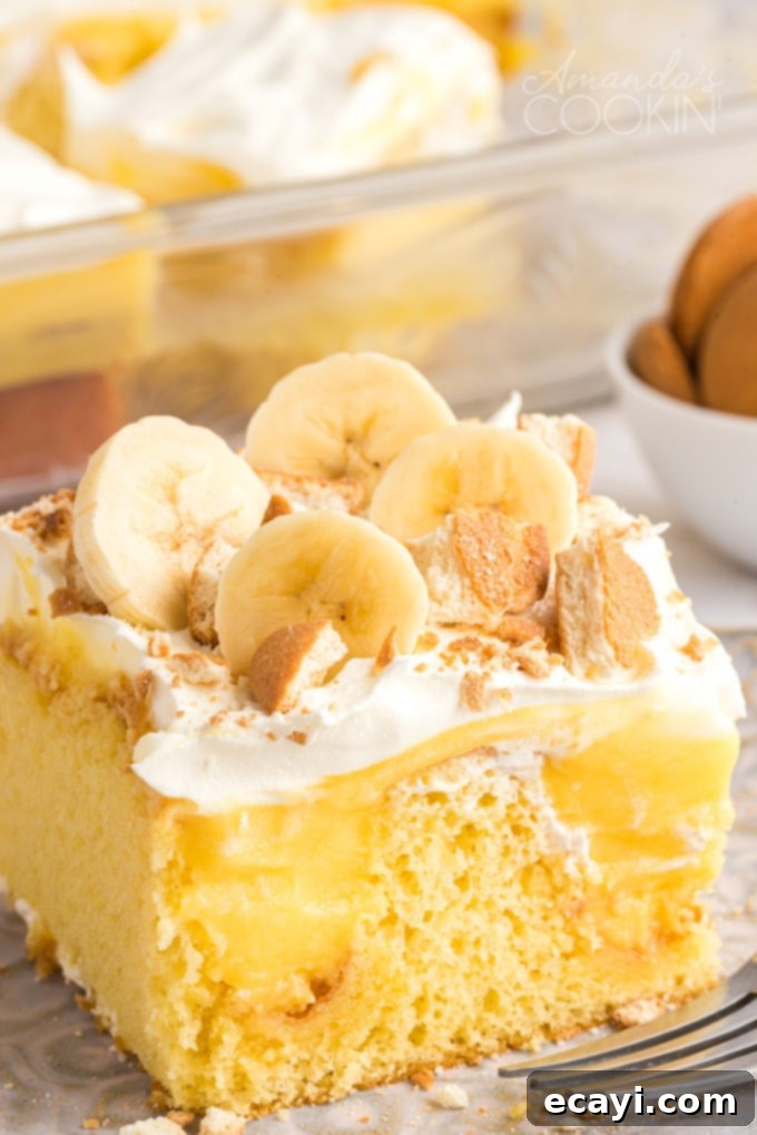 This delicious banana pudding poke cake recipe is quick and easy and perfect for a potluck. Use a cake mix for this beautiful poke cake dessert! Close up photo of a slice of banana pudding poke cake, showing layers of cake, pudding, whipped cream, and bananas with Nilla wafers